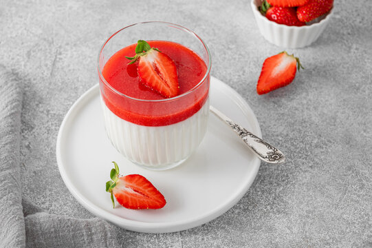 Traditional Italian dessert panna cotta or mousse with strawberry sauce and fresh berries on top in a glass jar.