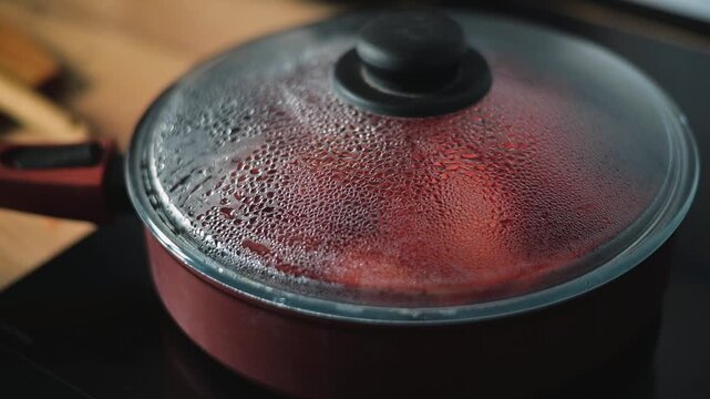 A covered pot sits on a stove, steam rising from its lid as food cooks inside. The kitchen environment shows various tools and a warm ambiance during meal preparation