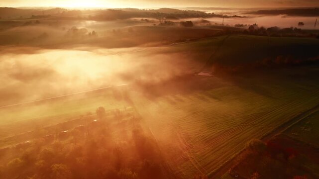 Aerial view of dramatic orange sunrise over misty landscape, with beautiful moody golden light illuminating the mist over the rural area