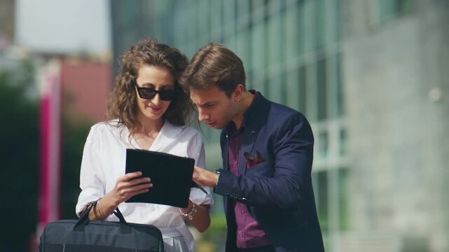 Two business professionals are having an outdoor meeting, discussing content on a digital tablet. These colleagues collaborate and interact while reviewing information outdoors.