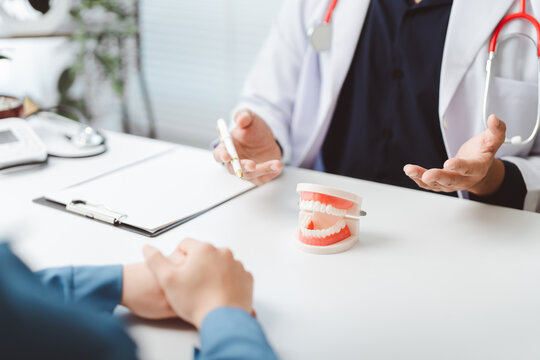 Dentist explaining oral health diagnosis and a dental treatment plan to a patient during a medical consultation, using a jaw model for better understanding in a clinic office