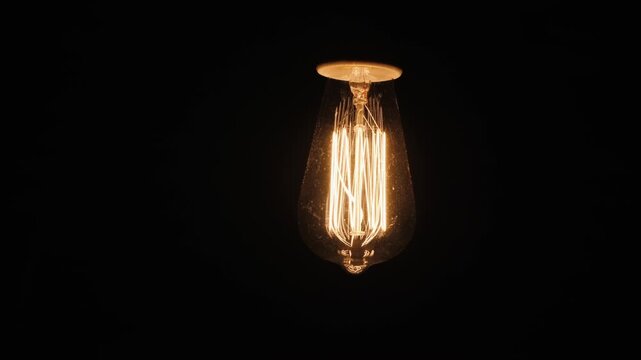Vintage edison light bulb illuminating dark room with warm glow and flickering filament capturing classic design.
