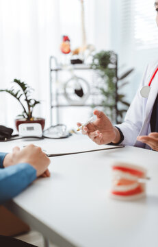 Dentist explaining endodontic and dental care treatment to patient in office, holding a tooth model during consultation, discussing oral health and hygiene