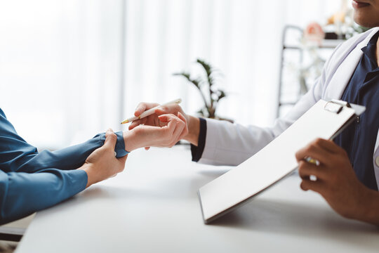 Medical professional examining patient's wrist, discussing symptoms and providing consultation during a physical check-up in a modern clinic setting