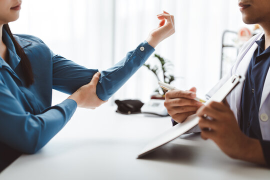 Woman experiencing elbow pain during medical consultation with doctor, receiving diagnosis and treatment advice for joint injury or orthopedic condition