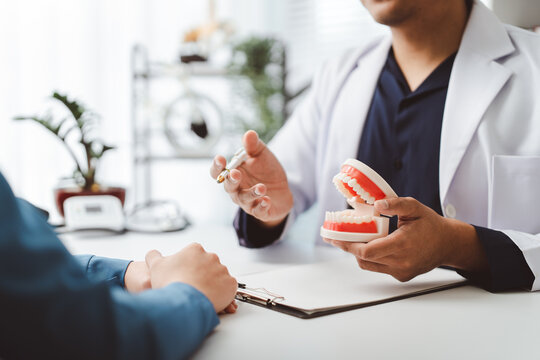 Dentist explaining complex dental procedure to patient, holding a jaw model and pointing with a pen, discussing effective treatment options in a modern clinic office