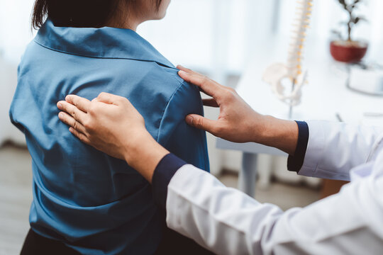 Doctor examining female patient's upper back, feeling for pain or discomfort, discussing symptoms related to spinal health and body wellness in medical clinic