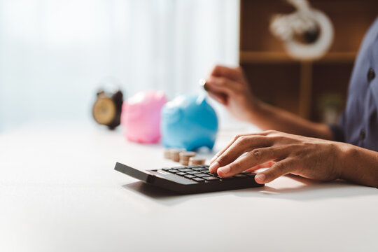 Person's hands calculating expenses and depositing coins into piggy bank, illustrating the concept of saving money, budgeting, and future financial planning