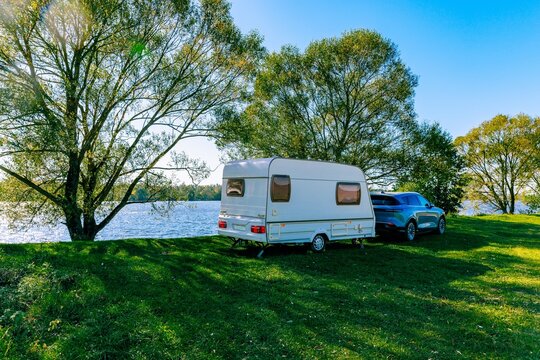 Caravan parked beside lake under green trees on clear sunny day with blue skies