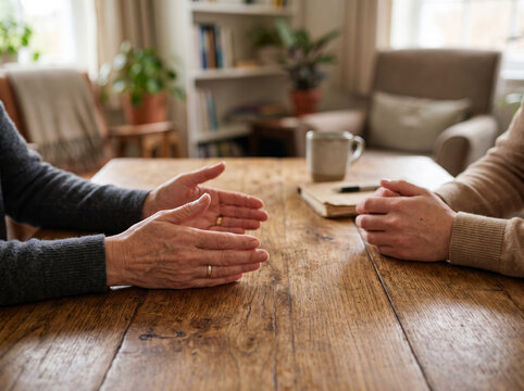 Therapy Session with Two People Holding Hands Across Wooden Table
