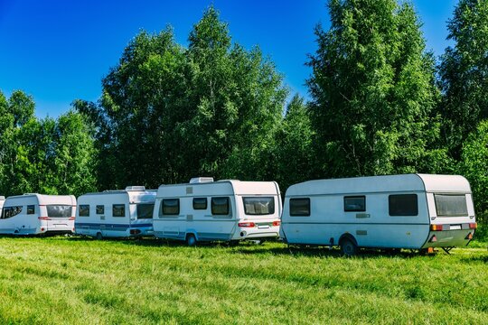 Caravans parked in green field under blue sky during sunny day with lush trees in background