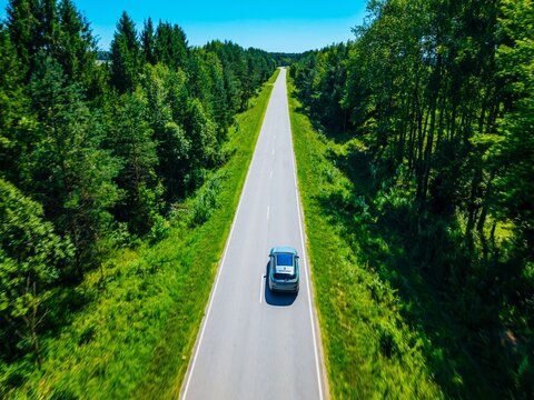 Aerial view of a car traveling down a straight road surrounded by lush green trees