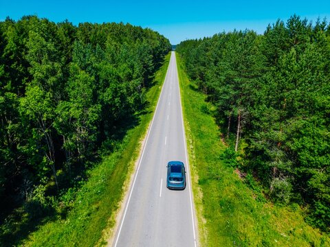 Car driving on a straight highway surrounded by lush green trees under a clear blue sky
