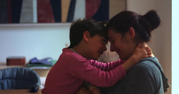 Mother and young son touch foreheads in loving embrace at home, expressing secure attachment, emotional connection and authentic family affection