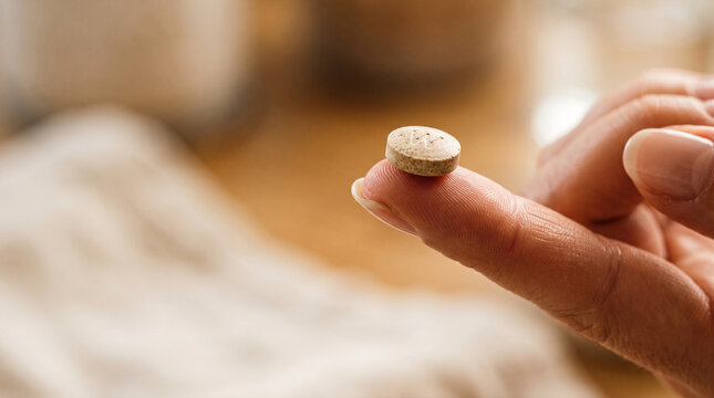 Close-up of human finger holding a small tan pill with visible inscription