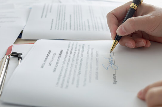 Close-up of hand holding metallic pen writing or signing document. Concept of business contract, legal approval, and education.