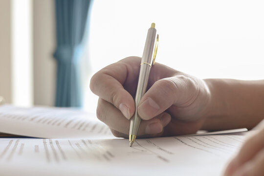 Close-up of hand holding metallic pen writing or signing document. Concept of business contract, legal approval, and education.