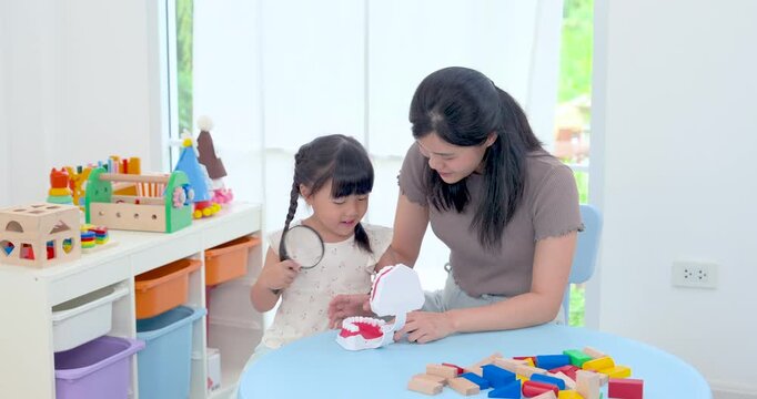 Asian single mother helping preschool daughter explore dental model during educational play, child touching mouth while learning tooth care, home development activity building trust, healthy habit