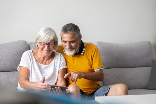 Senior couple using smartphone together on sofa at home. Copy space