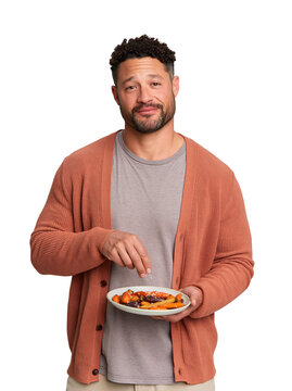Smiling man seasoning roasted carrots on a plate against isolated on transparent or white background, png