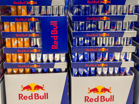 Berlin, Germany July 29, 2026. Stacked cases of Red Bull energy drinks fill a store display in orange and blue varieties. Cans of the Apricot Edition and Blue Edition line the shelves alongside the or