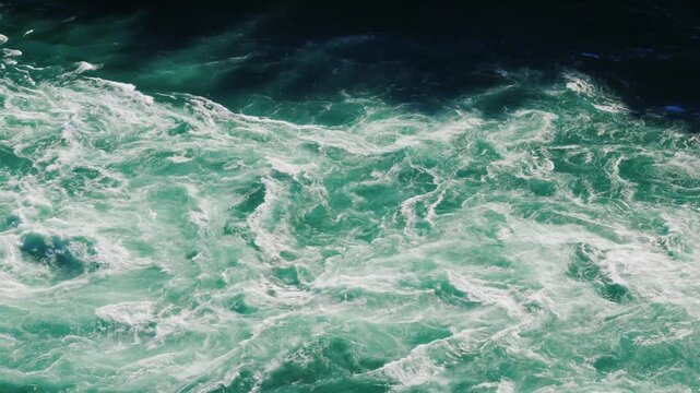 Turbulent river water flows rapidly, creating foamy white rapids and mesmerizing natural abstract patterns with dynamic liquid motion.