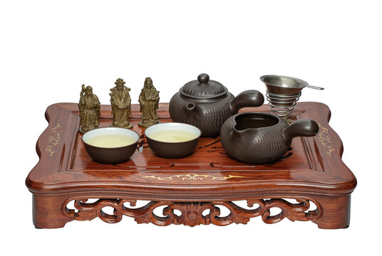 Traditional Chinese tea set with clay teapot fair cup tea cups strainer and three small metal statues on wooden chaban tray isolated on white background.