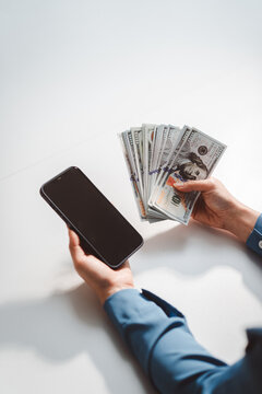 Person holding smartphone and hundred-dollar bill, illustrating mobile banking, cash transactions, budgeting and personal finance with digital and traditional payment methods