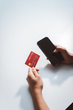 Person's hands holding red credit card and mobile phone, performing secure online payment, purchasing items, and managing financial transactions digitally