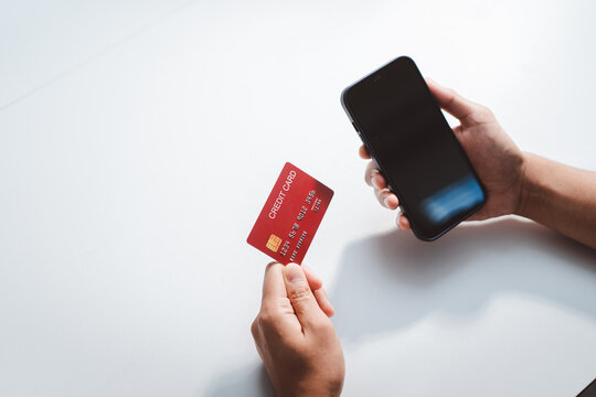 Person holding a red credit card and a blank screen smartphone, representing secure online shopping, mobile banking, digital payment, e-commerce, and financial transaction concepts