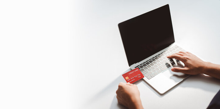 Person typing on laptop keyboard, holding red credit card, making online purchase, secure e-commerce, digital payment transaction on white table background