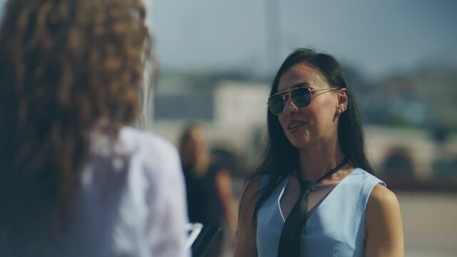 Two businesswomen engage in an outdoor discussion, collaborating professionally. An outdoor business meeting takes place between two female colleagues.