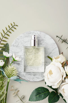 Glass perfume bottle on marble tray with white roses and green leaves decoration on beige background. copy space