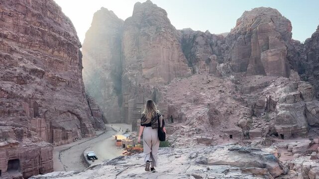 Breathtaking footage of a woman making her way to a dramatic vantage point high above Petra, revealing sweeping views over the extraordinary ancient ruins of one of the world's greatest archaeological