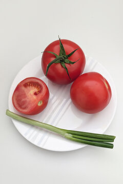 Fresh tomatoes and green onions on a white plate ready for cooking or serving at home kitchen