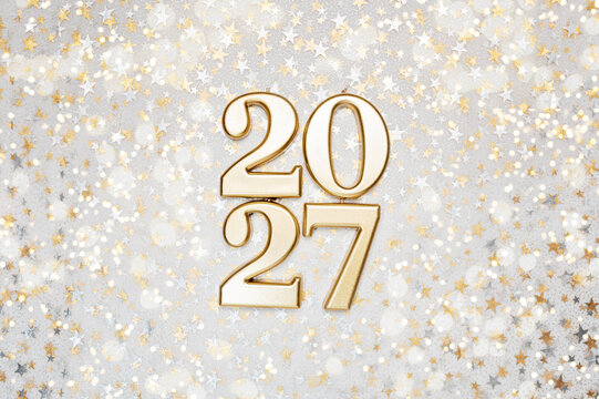 Holiday background Happy New Year 2027. Numbers of year 2027 made by burning gold candles on red festive sparkling background.