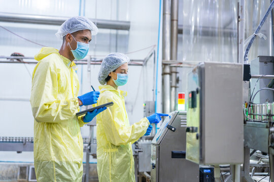 Quality control inspectors operating machinery in a food factory, Factory workers in protective suits checking control panel, Industrial team monitoring automated production line in clean plant