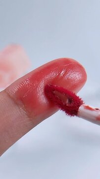 Applying rosy red color on fingertip using a brush. Extreme vertical close up with soft blurred white background. Beauty makeup application concept.