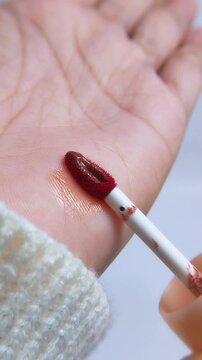 Process of trying or testing lip tint color on hand skin using a red brush. Front vertical capture. Beauty product concept for makeup swatch demo.