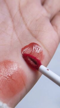 Process of applying lip tint color on palm. Vertical close up capture. Suitable for beauty product advertisement concept, cosmetic swatch demo.