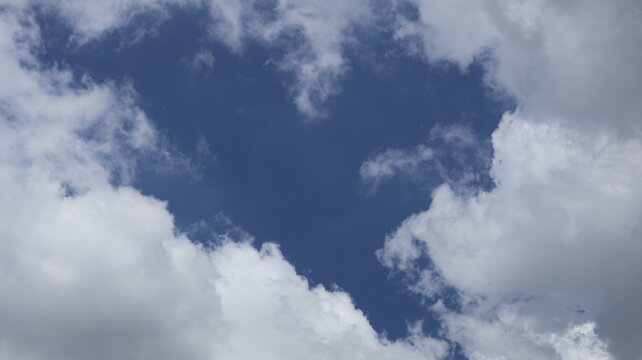 The image depicts a section of the sky with scattered clouds. The clouds are mostly white and fluffy, with some variations in density and shape