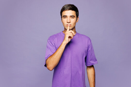 Young secret Caucasian man he wear violet t-shirt casual clothes say hush be quiet with finger on lips shhh gesture isolated on plain pastel light purple background studio portrait. Lifestyle concept.