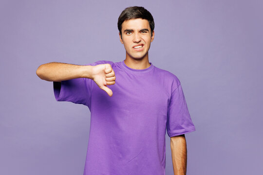 Young sad displeased dissatisfied Caucasian man he wear violet t-shirt casual clothes showing thumb down dislike gesture isolated on plain pastel purple background studio portrait. Lifestyle concept.