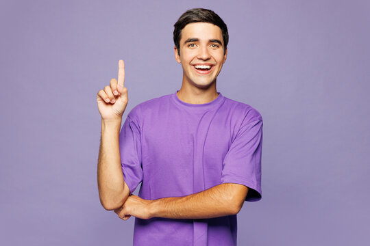 Young smiling happy Caucasian man he wears violet t-shirt casual clothes point index finger aside on area mock up isolated on plain pastel light purple background studio portrait. Lifestyle concept.