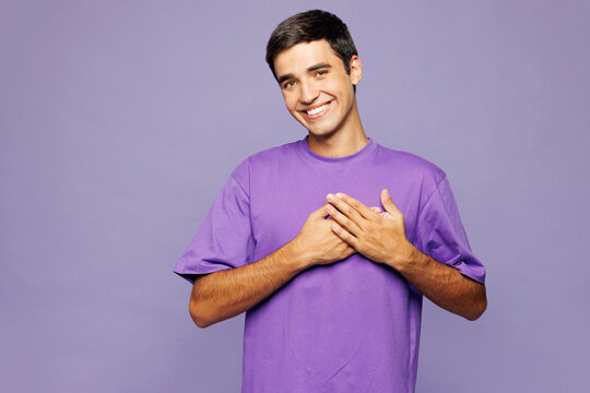 Young smiling happy fun Caucasian man he wear violet t-shirt casual clothes put folded hands on heart look camera isolated on plain pastel light purple background studio portrait. Lifestyle concept.