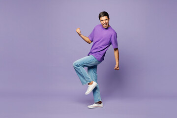 Full body young man wears violet t-shirt casual clothes doing winner gesture celebrate clenching fists say yes raise up leg isolated on plain pastel light purple background studio. Lifestyle concept. © ViDi Studio