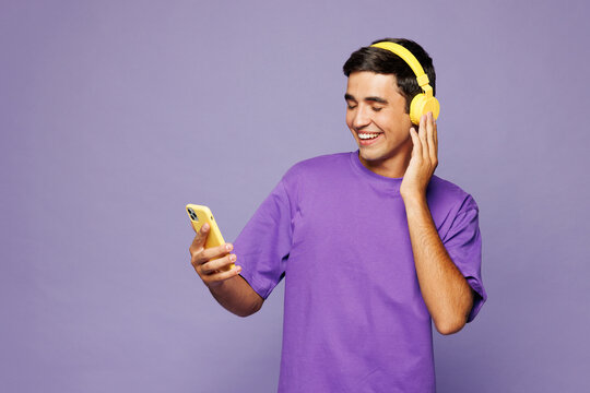 Young man he wear violet t-shirt casual clothes listen to music in headphones hold use mobile cell phone record voice sing isolated on plain pastel light purple background studio. Lifestyle concept.