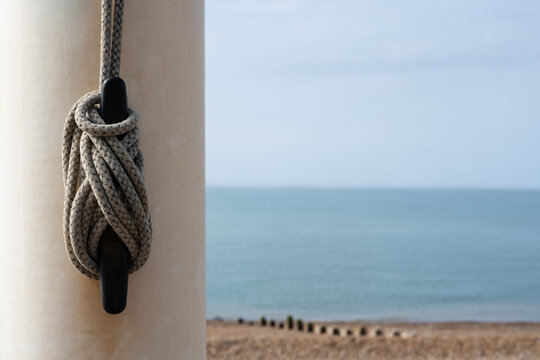 Coiled flag rope attached to a beach flagpole with pebble shoreline and calm blue sea forming a versatile coastal background for travel, summer and seaside design projects