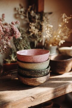 Warm kitchen shelf displaying stacked coral ceramic bowls, dried botanicals, fresh herbs, and inviting rustic decor