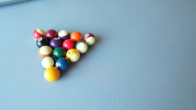 Cue ball striking a tightly racked triangle of billiard balls on a blue felt table, capturing the powerful opening break that marks the start of a competitive pool game.